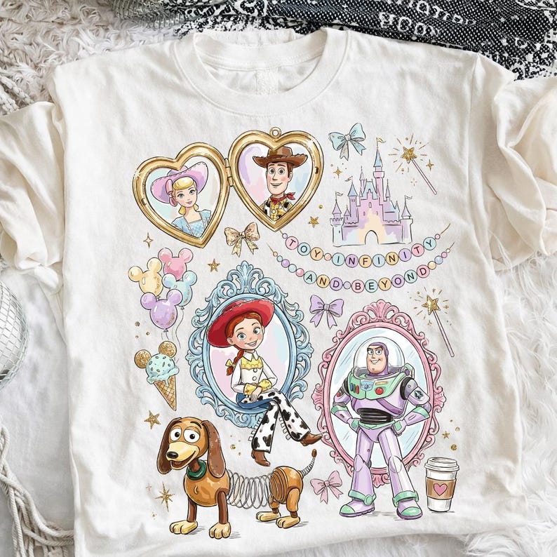 Może przedstawiać: Biała koszulka z kolorowymi ilustracjami postaci z Toy Story, w tym Chudego, Buzz'a Astrala i Jessie, w ozdobnych ramkach. Projekt zawiera zamek, balony i napis "TO INFINITY AND BEYOND."