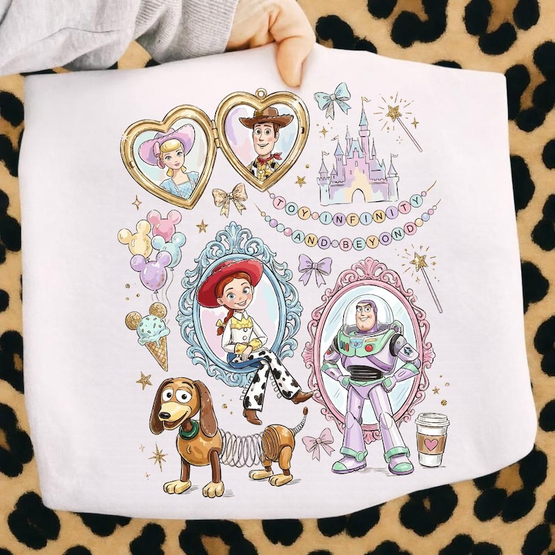 Może przedstawiać: Biała tkanina z ilustracjami postaci z Toy Story, w tym Woody, Buzz Lightyear i Jessie, w ozdobnych ramkach. Zawiera r&oacute;wnież napis "TO INFINITY AND BEYOND".
