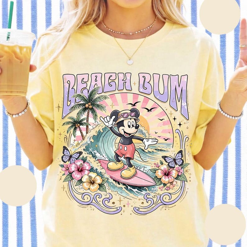 May include: Yellow t-shirt with a graphic of Mickey Mouse surfing, the text "BEACH BUM", palm trees, waves, butterflies, and flowers. The design features a retro, vintage style with a pastel color palette.