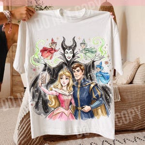 May include: White t-shirt with a vibrant illustration of fairy tale characters. The design includes a princess, a prince, and a villain, along with several fairies. The text "ORIGINAL DESIGNER CALIGRAPHICDESIGN" is printed at the top.
