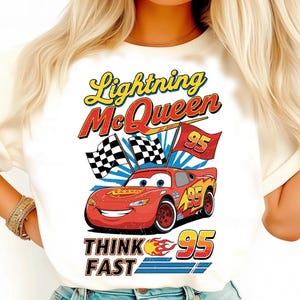 May include: White t-shirt featuring Lightning McQueen from the Cars movie. The design includes the text "Lightning McQueen" in yellow and red, the number "95", and the phrase "Think Fast". Checkered flags and a red race car are also featured.