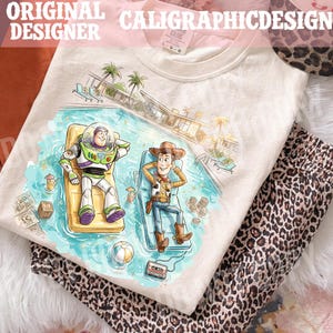 May include: Cream-colored t-shirt featuring a cartoon illustration of Buzz Lightyear and Woody relaxing by a pool. The shirt has the text "ORIGINAL DESIGNER CALIGRAPHICDESIGN" at the top. Leopard print pajama pants are folded next to the shirt.