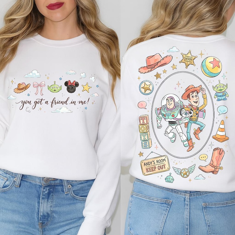 May include: White sweatshirt featuring a colorful design with the text "you got a friend in me!". The design includes cartoon characters, a cowboy hat, and a sheriff's badge. The back of the sweatshirt has a large graphic of cartoon characters.