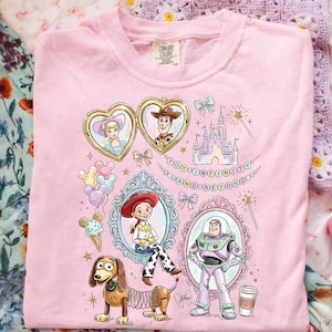 Może przedstawiać: R&oacute;żowa koszulka Comfort Colors z ilustracjami postaci z Toy Story Disneya. Zawiera wizerunki Woody'ego, Buzza Astrala, Jessie i Slinky'ego, a także zamek, kokardy i napis "TOY AND BEYOND".