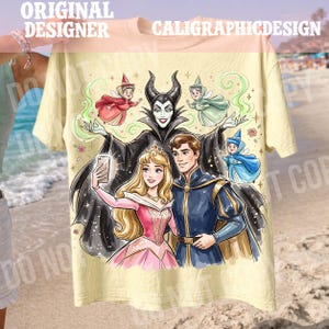 May include: A light yellow t-shirt with a colourful illustration of fairy tale characters. The design includes a princess, a prince, and a villain taking a selfie, with fairies and the text "ORIGINAL DESIGNER CALIGRAPHICDESIGN".