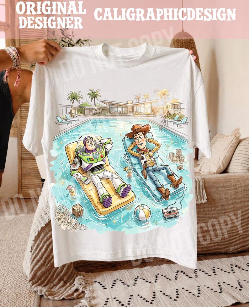 May include: White t-shirt featuring a colorful illustration of Buzz Lightyear and Woody relaxing in a pool. The design includes a pool scene with palm trees, a building, and various accessories. The text "ORIGINAL DESIGNER CALIGRAPHICDESIGN" is at the top.