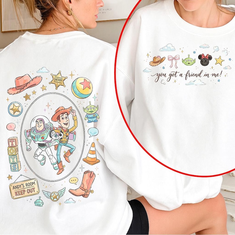 May include: White sweatshirt featuring colorful cartoon graphics of characters and icons from a popular animated movie. The design includes a cowboy hat, a sheriff's badge, and the text "you got a friend in me!" on the front. The back has more graphics and the text "ANDY'S ROOM KEEP OUT".