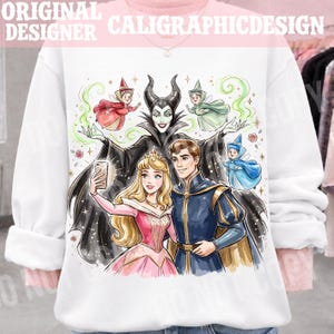 May include: White sweatshirt with a vibrant illustration of fairy tale characters. The design includes a princess, a prince, fairies, and a villain taking a selfie. The text "ORIGINAL DESIGNER CALIGRAPHICDESIGN" is at the top.