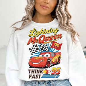 May include: White sweatshirt featuring a graphic of Lightning McQueen from the Cars movie. The design includes the text "Lightning McQueen", "95", "Think Fast", and checkered flags. The car is red and yellow.
