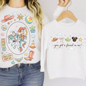 May include: White sweatshirts with colorful Toy Story graphics. One sweatshirt features Buzz Lightyear and Woody in an oval frame, surrounded by other Toy Story elements. The other sweatshirt has the text "you got a friend in me!" with other Toy Story characters.