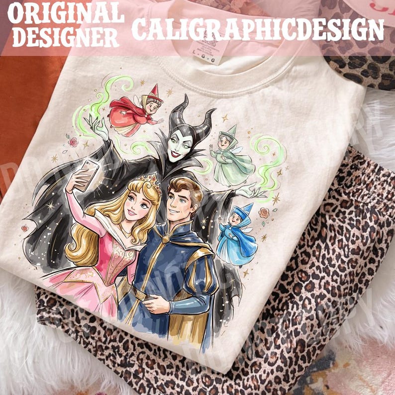 May include: Cream-coloured t-shirt with a colourful illustration of fairy tale characters. The design includes a princess, a prince, fairies, and a villain taking a selfie. The text "ORIGINAL DESIGNER CALIGRAPHICDESIGN" is at the top.