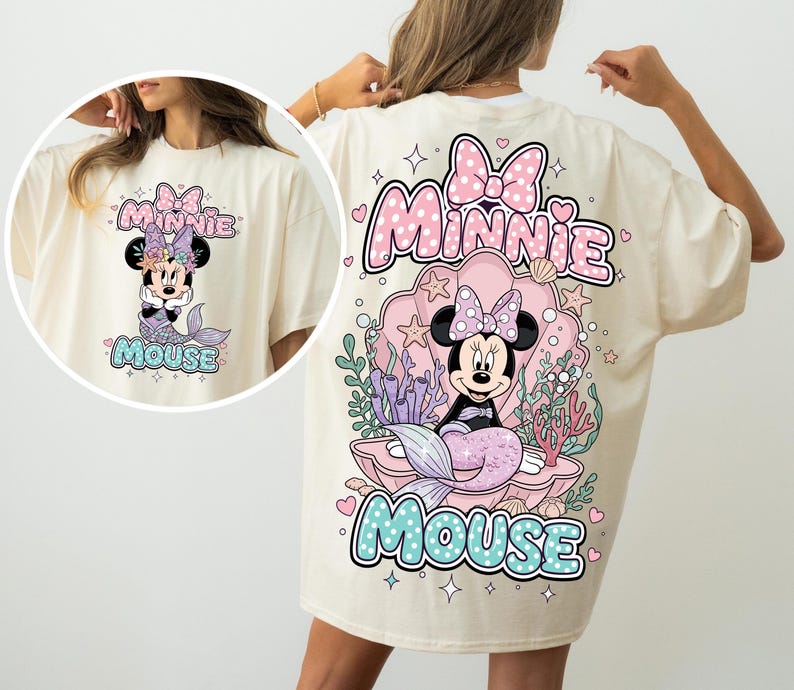 May include: Cream-colored t-shirt featuring a Minnie Mouse mermaid design. The graphic includes a pink bow, the words "Minnie Mouse", and a mermaid tail. The design is repeated on the front of the shirt.