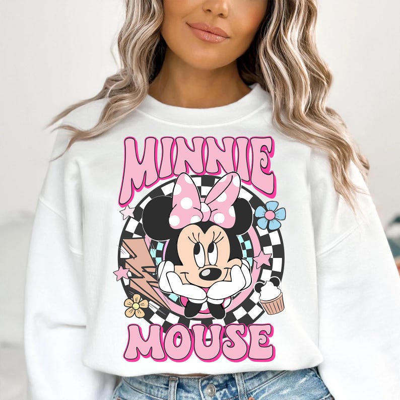 May include: White sweatshirt featuring a retro-style Minnie Mouse graphic. The design includes Minnie's face, a pink bow, and the words "MINNIE MOUSE" in pink bubble letters. The graphic is set against a black and white checkered background.
