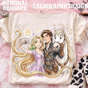 May include: Cream-colored t-shirt featuring a cartoon illustration of a princess, a man, and a white horse taking a selfie. The princess has long blonde hair and is wearing a purple dress. The text "ORIGINAL DESIGNER CALIGRAPHICDESIGN" is at the top.