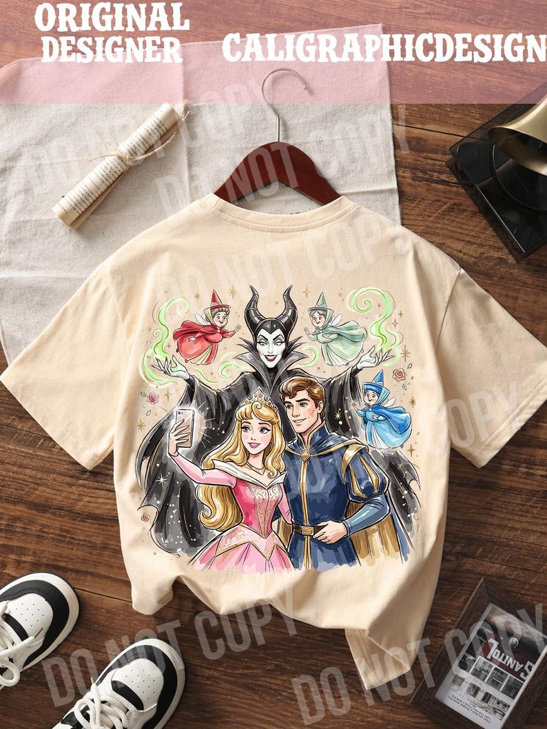 May include: A beige t-shirt with a colourful illustration of fairy tale characters. The design shows a princess, a prince, and a villain taking a selfie, with the text "ORIGINAL DESIGNER CALIGRAPHICDESIGN" at the top.