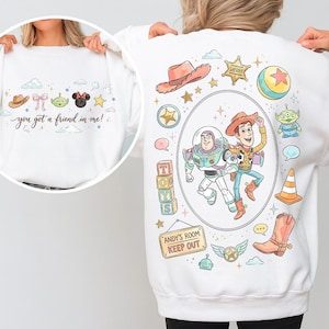 May include: White sweatshirt featuring cartoon characters and the phrase "you got a friend in me!". The design includes a cowboy hat, bow, alien, Minnie Mouse, and stars. The back features Buzz Lightyear and Woody, along with other Toy Story themed graphics.