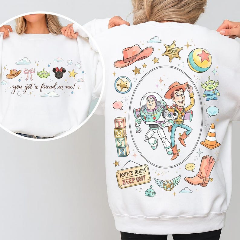 May include: White sweatshirt featuring cartoon characters and the phrase "you got a friend in me!". The design includes a cowboy hat, bow, alien, Minnie Mouse, and stars. The back features Buzz Lightyear and Woody, along with other Toy Story themed graphics.