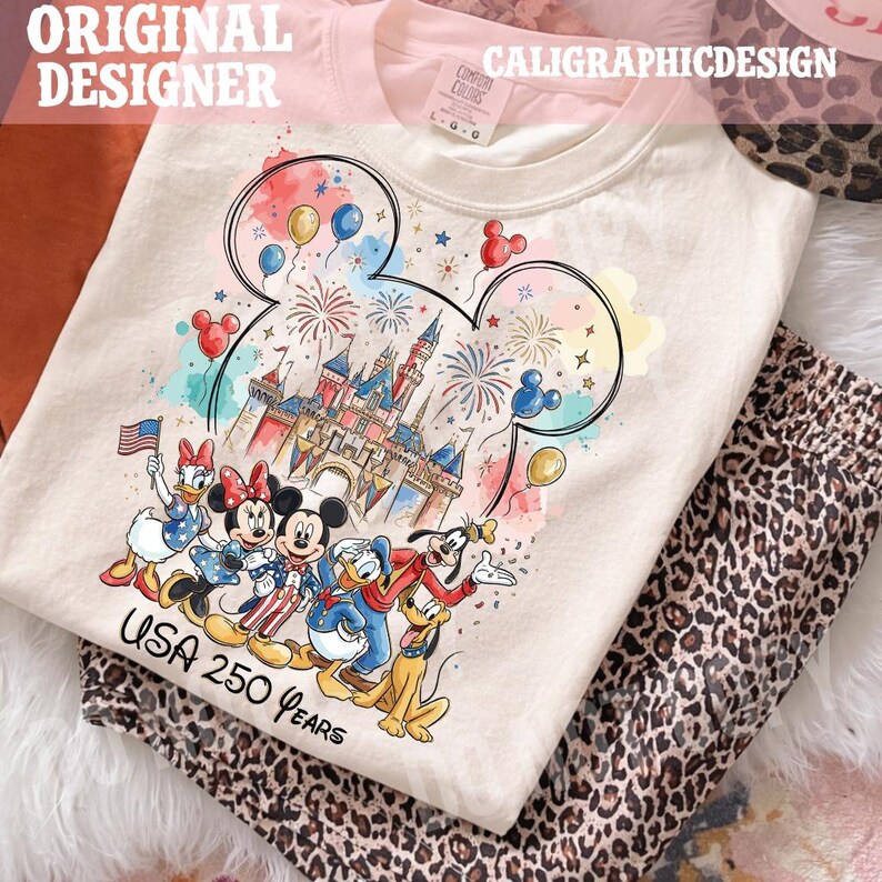 May include: Cream-colored t-shirt featuring a colorful graphic of Disney characters, a castle, fireworks, and balloons. The text "USA 250 Years" is printed below the characters. The shirt is paired with leopard print pants.