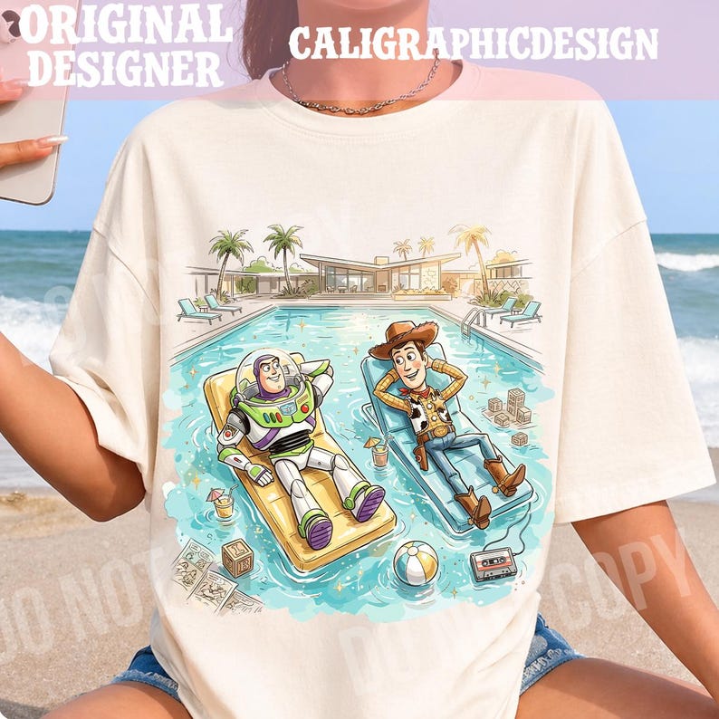 May include: Cream-colored t-shirt featuring a cartoon illustration of Buzz Lightyear and Woody relaxing by a pool. The image includes the text "ORIGINAL DESIGNER" and "CALIGRAPHICDESIGN". The scene is set at a resort with palm trees and a beach.