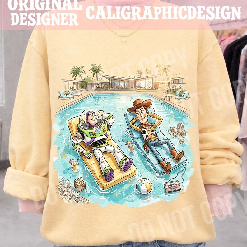 May include: A light yellow sweatshirt featuring a cartoon illustration of Buzz Lightyear and Woody relaxing by a pool. The image includes a mid-century modern house, palm trees, and pool accessories. The text "ORIGINAL DESIGNER CALIGRAPHICDESIGN" is at the top.