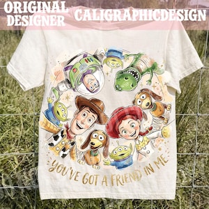 以下が含まれることがあります： オフホワイトのTシャツ。人気アニメ「トイ・ストーリー」のキャラクターたちが描かれたカラフルなイラストが特徴。ウッディ、バズ・ライトイヤー、ジェシーなどが描かれ、「You've Got a Friend in Me」の文字が金色でデザインされています。半袖のTシャツです。
