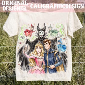 May include: Cream t-shirt with a colourful illustration of fairy tale characters. The design shows a princess, a prince, and a villain taking a selfie, with fairies and the text "ORIGINAL DESIGNER CALIGRAPHICDESIGN".