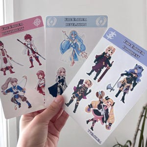 May include: Three sticker sheets featuring characters from the Fire Emblem video game series. The sheets are labeled "Birthright," "Revelation," and "Conquest." Each sheet has multiple character illustrations in various poses, with a color scheme of pink, blue, and purple.