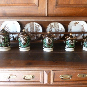 May include: Six brown ceramic canisters with green and white floral designs and gold accents. The canisters are labeled "Cafe", "Sucre", "The", "Poivre", and "Cafe".