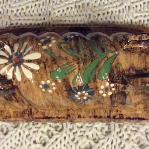 May include: A brown ceramic bread loaf pan with a twisted design. The pan is decorated with white, green, and blue floral patterns.