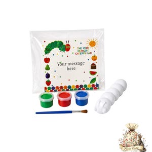 May include: A craft kit featuring a white caterpillar figure, three paint pots in green, red, and blue, and a paintbrush. The kit includes a clear bag with a colorful card featuring text from "The Very Hungry Caterpillar". The card reads "Your message here".