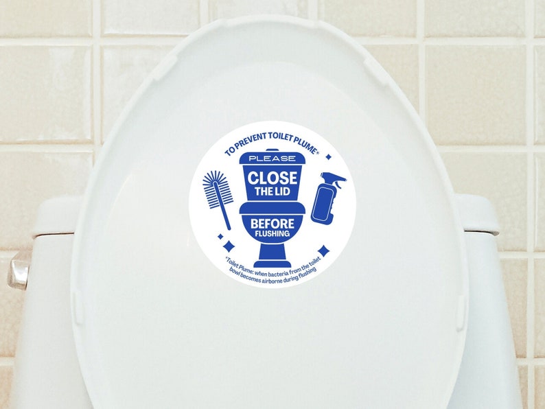 May include: A white toilet bowl with a blue and white sticker that says "To prevent toilet plume - Please close the lid before flushing". The sticker also shows a toilet bowl with a toilet brush and a spray bottle.