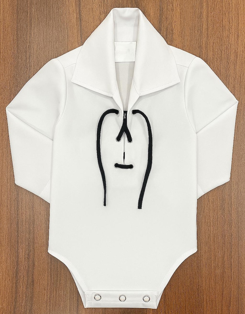 May include: White baby bodysuit with long sleeves and a collared neckline. The front features a black decorative design. The bodysuit has three snap closures at the bottom. The garment is made of a soft, comfortable material.