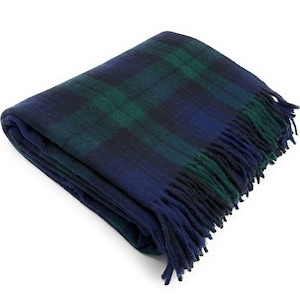 Può includere: Coperta piegata a quadri blu navy e verde. La coperta presenta un classico motivo tartan e un bordo con frange. Il materiale morbido e tessuto è visibile in primo piano. Questa coperta è ideale per aggiungere calore e stile a qualsiasi spazio.