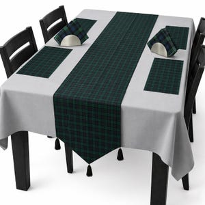 May include: A light gray tablecloth featuring a dark green and navy blue plaid table runner with black tassels at the ends. The set includes matching rectangular plaid placemats and folded plaid napkins held in silver-toned metal napkin holders.