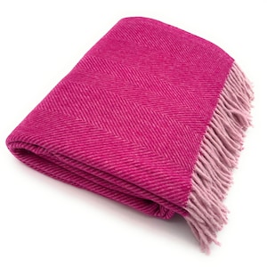 Op de afbeelding: Een opgevouwen magenta deken met een visgraatpatroon. De deken heeft een franje in een lichtere roze tint langs één rand. De deken is gemaakt van een zacht, geweven materiaal.