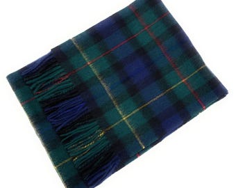 May include: A rectangular scarf with a plaid pattern in shades of blue, green, and black, accented with thin red and yellow lines. The scarf has a fringed edge in blue and green. The scarf is made of a soft material.