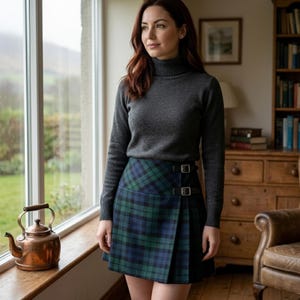 Può includere: Un maglione a collo alto grigio antracite a maniche lunghe abbinato a una gonna a portafoglio al ginocchio con motivo a quadri blu e verde, un pannello laterale plissettato e due fibbie in metallo argentato sulla cintura anteriore.