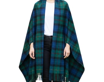 May include: A green and blue plaid cape with fringe along the bottom edge. The cape is draped over a person wearing a white shirt and black pants. The plaid pattern includes black and red lines.