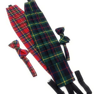 May include: Two plaid cummerbunds in red and green, with matching bow ties. The cummerbunds are rectangular with a pleated design. The bow ties are pre-tied. Black suspenders are attached to the green cummerbund. The background is white.