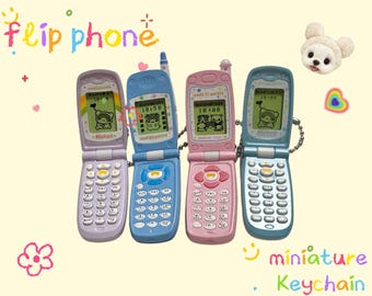 May include: Four miniature flip phone keychains in pastel colors: lavender, blue, pink, and teal. Each phone has a small screen displaying a cartoon character and the time. The word "flip phone" is written above the phones.