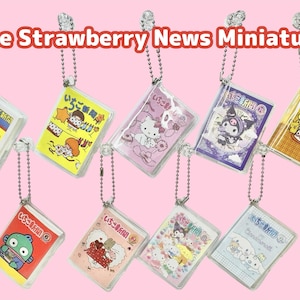 以下が含まれることがあります： 様々な漫画のキャラクターとデザインが特徴の、ミニチュア「The Strawberry News」キーホルダー。各キーホルダーは、カラフルなグラフィックとシルバーチェーンが付いた小さな透明プラスチックケースに入っています。「The Strawberry News Miniature」の文字が上部にあります。