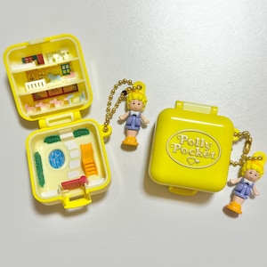 Może przedstawiać: Dwa ż&oacute;łte kompakty Polly Pocket, jeden otwarty, aby odsłonić miniaturowe wnętrze z meblami i lalką. Drugi kompakt jest zamknięty ze słowami "Polly Pocket". Każdy ma dołączoną lalkę.