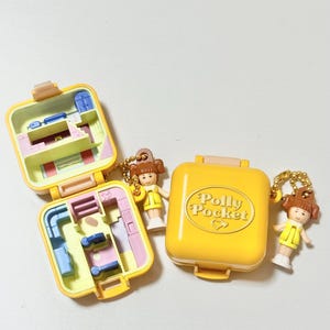 May include: Yellow Polly Pocket compact with the text "Polly Pocket" and two miniature figures. Two open compacts reveal interior rooms. The figures are wearing yellow dresses. The compacts are on a white surface.