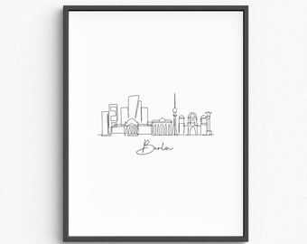 May include: A framed black and white line art print of the Berlin skyline. The minimalist illustration features iconic buildings and landmarks, with the city name, "Berlin," written in cursive below the skyline.