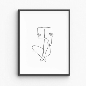 Puede incluir: Lámina artística minimalista enmarcada en negro que presenta un dibujo de línea continua de una persona leyendo un libro. La obra de arte representa a una persona sentada con las piernas cruzadas, sosteniendo un libro abierto frente a su rostro. El diseño es simple y elegante.