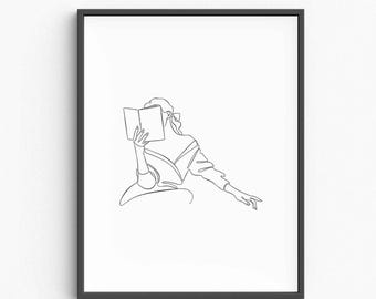 May include: Black framed art print featuring a minimalist line drawing of a person reading a book. The artwork is a continuous line illustration, depicting a figure in a dress with an open book, and a relaxed pose. The print is on a white background.