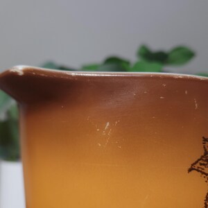 May include: Close-up of a vintage Pyrex mixing bowl with a brown and orange gradient. The bowl has a pouring spout and a decorative pattern. The bowl shows signs of wear, adding to its vintage charm.