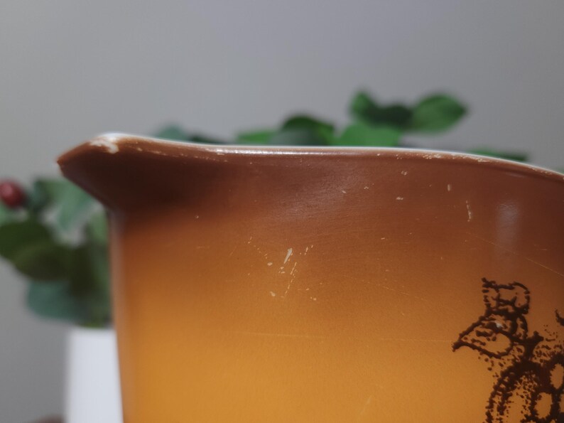 May include: Close-up of a vintage Pyrex mixing bowl with a brown and orange gradient. The bowl has a pouring spout and a decorative pattern. The bowl shows signs of wear, adding to its vintage charm.