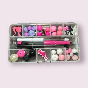 May include: A clear plastic organizer filled with various craft supplies. The organizer contains pens, beads, and decorative silhouette charms in shades of pink, white, black, and purple. The beads are in various shapes and sizes.