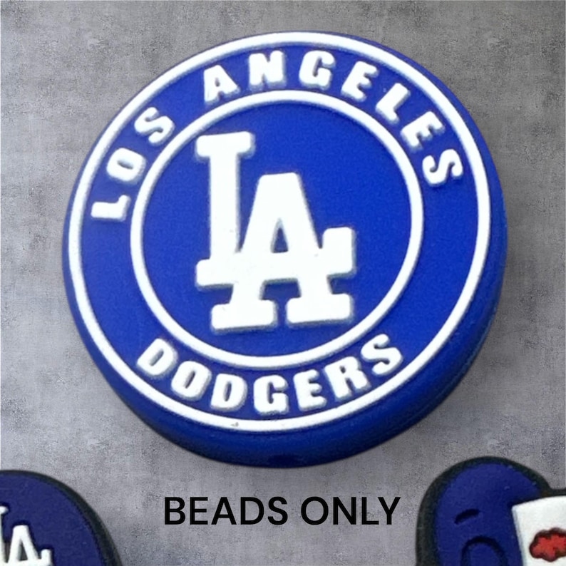 May include: A blue and white Los Angeles Dodgers logo bead. The bead is round with the words "LOS ANGELES DODGERS" in white around the edge. The center features the team's "LA" logo in white. The text "BEADS ONLY" is below the bead.